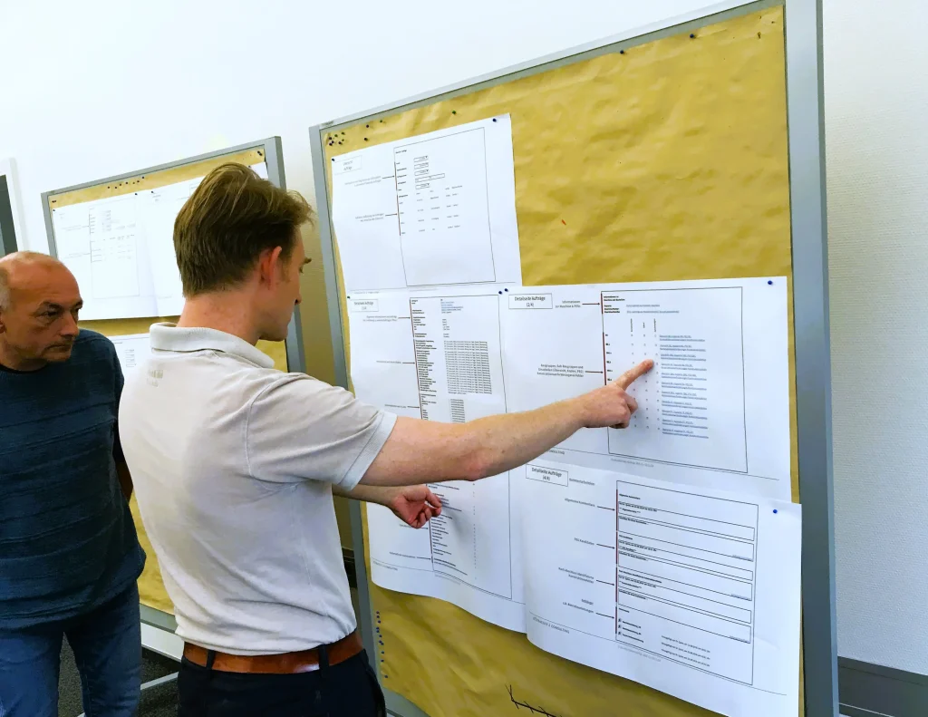 Zwei Männer schauen sich Papiere auf einer Pinwand an